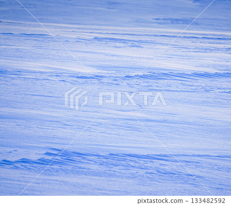 A cold-looking scene of a snowy field near sunset, with wind ripples visible 133482592
