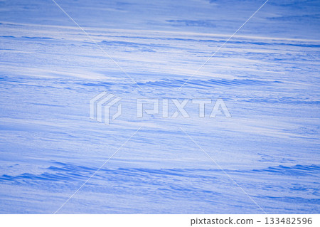 A cold-looking scene of a snowy field near sunset, with wind ripples visible A cold-looking scene of a snowy field near sunset, with wind ripples visible 133482596