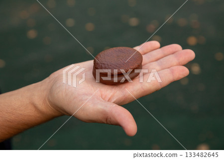 Airy sponge cake with delicate cream inside, covered in chocolate glaze in man hand. small round sponge cake with chocolate. 133482645