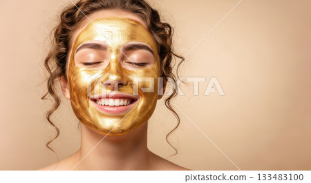 Woman with golden facial mask smiles joyfully, showcasing skincare routine and self-care concept against a neutral background with soft lighting 133483100