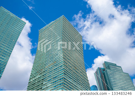 Modern turquoise glass towers skyscrapers on blue cloudy sky, view from below from street. glass facade and contemporary design. Modern turquoise glass towers skyscrapers on blue cloudy sky, view from below from street. glass facade and contemporary design. 133483246