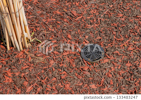 Root irrigation system. plastic lid of irrigation system on Rubber mulch imitating wood chips coating. trunk of a young tree 133483247