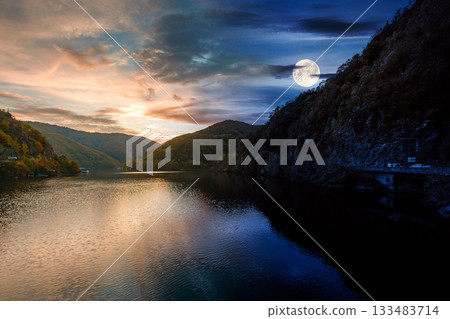 mountainous landscape with lake on autumn equinox. day and night time change concept. forest on hills near the shore of river under sky with moon at twilight. beautiful view of stunning place mountainous landscape with lake on autumn equinox. day and night time change concept. forest on hills near the shore of river under sky with moon at twilight. beautiful view of stunning place 133483714