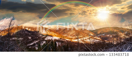 winter panorama of forested mountains with snowy tops under cloudy sky at sunset. wonderful nature landscape for banner or flyer background in evening light. timeless nostalgia book cover with rainbow winter panorama of forested mountains with snowy tops under cloudy sky at sunset. wonderful nature landscape for banner or flyer background in evening light. timeless nostalgia book cover with rainbow 133483718