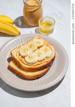 Peanut butter sandwich and banana on a plate on a marble background with fruits and honey. Peanut butter sandwich and banana on a plate on a marble background with fruits and honey. 133483724