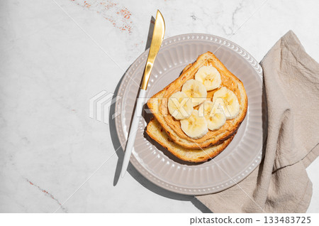 Peanut butter sandwich and banana on a plate on a marble background with knife and napkin. 133483725