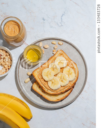 Peanut butter toast and banana on a plate on a marble background with fruits Peanut butter toast and banana on a plate on a marble background with fruits 133483726