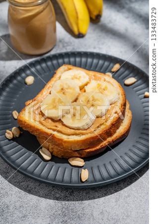 Peanut butter toast and banana on a black plate on a gray background with nuts 133483729
