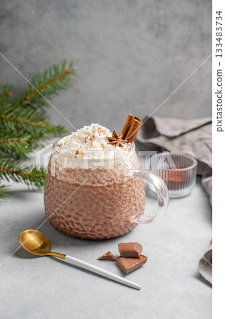 Hot chocolate with wipped cream in a cup on a light background with fir branches and spoon. Hot chocolate with wipped cream in a cup on a light background with fir branches and spoon. 133483734