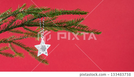 Fir branches with a star-shaped Christmas tree ornament on a red background close up. 133483738