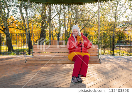 A body positive woman sits on swing and drinks coffee. A 47-year-old Caucasian woman, mother of many children, relaxes alone on a bright autumn day. Mental health, harmony with oneself and the world A body positive woman sits on swing and drinks coffee. A 47-year-old Caucasian woman, mother of many children, relaxes alone on a bright autumn day. Mental health, harmony with oneself and the world 133483898