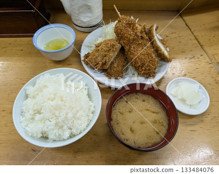 一張桌子上擺著米飯,上面蓋著豬排;一個咖哩鍋裡盛著麵糊,還有各種配料。 一張桌子上擺著米飯,上面蓋著豬排;一個咖哩鍋裡盛著麵糊,還有各種配料。 133484076