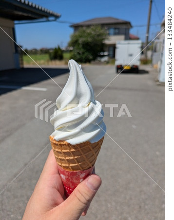 Holding a soft serve ice cream in hand, blue sky background 133484240
