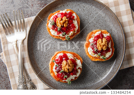 Delicious baked sweet potato with cream cheese, cranberry sauce, thyme and walnuts close-up in a plate. Horizontal top view Delicious baked sweet potato with cream cheese, cranberry sauce, thyme and walnuts close-up in a plate. Horizontal top view 133484254