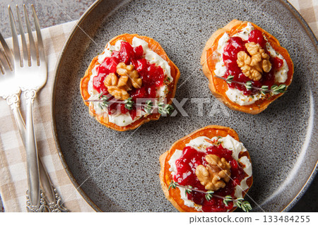 festive sweet potato appetizer with cream cheese, cranberry sauce, thyme and walnuts close-up in a plate. Horizontal top view festive sweet potato appetizer with cream cheese, cranberry sauce, thyme and walnuts close-up in a plate. Horizontal top view 133484255