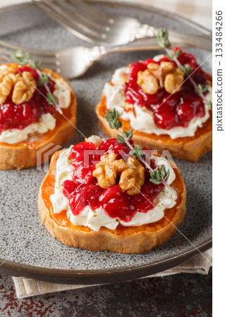 Baked sweet potato with cream cheese, cranberry jam and walnuts close-up in a plate. Vertical 133484266