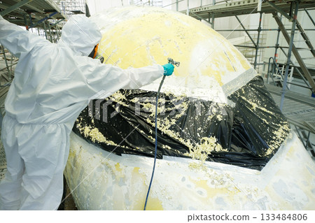 Worker applies protective coating to aircraft surface inside hangar during maintenance procedures at aerospace facility Worker applies protective coating to aircraft surface inside hangar during maintenance procedures at aerospace facility 133484806