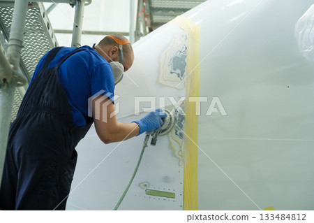 Worker prepares aircraft surface for painting in a hangar during day 133484812