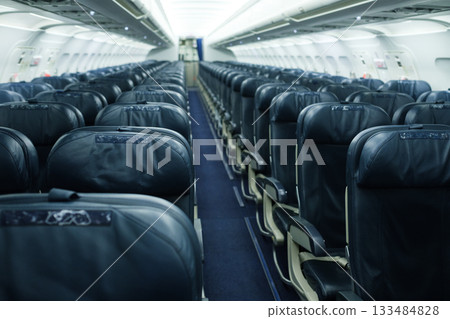 Passenger airplane interior showing rows of empty seats ready for boarding during a flight preparation in a modern airport terminal 133484828