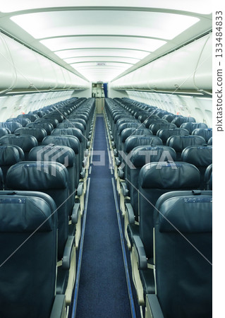 Empty airplane cabin with rows of leather seats and an aisle leading to the front in a modern commercial plane during daytime 133484833