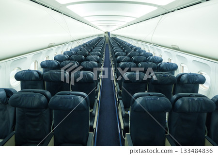 Empty airplane interior showcasing rows of dark blue seats from the front towards the back during a quiet flight Empty airplane interior showcasing rows of dark blue seats from the front towards the back during a quiet flight 133484836