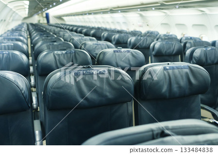 Empty airplane interior showing rows of black leather seats arranged neatly in a modern aircraft during a flight preparation phase 133484838