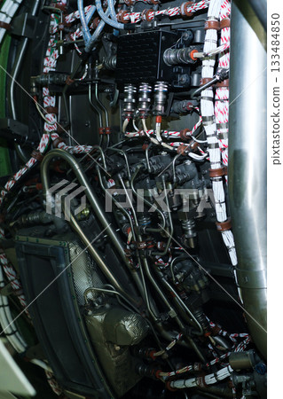 Detailed view of aircraft engine wiring and plumbing inside a maintenance hangar during the daytime, showcasing complex systems and components 133484850
