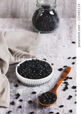 Raw black beans in a bowl and in a spoon on the table vertical view Raw black beans in a bowl and in a spoon on the table vertical view 133485114