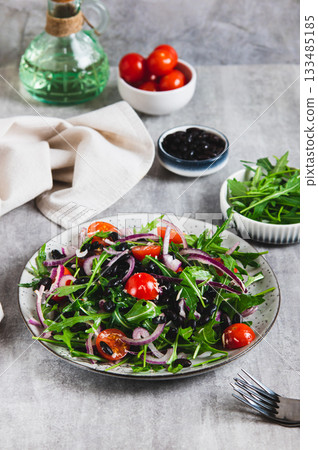 Fresh salad with black beans, cherry tomatoes, arugula and red onion on a plate vertical view 133485185