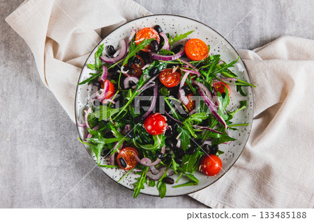Close up of fresh salad with black beans, cherry tomatoes, arugula and red onion on a plate top view Close up of fresh salad with black beans, cherry tomatoes, arugula and red onion on a plate top view 133485188