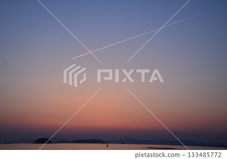 平靜的海面，夕陽西下，天空中劃過一道道凝結尾跡。 133485772
