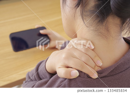A woman operating a smartphone with pain in her neck and shoulders A woman operating a smartphone with pain in her neck and shoulders 133485834