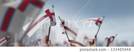 Faroe Islands flags in their hands on a blurred urban background Faroe Islands flags in their hands on a blurred urban background 133485848