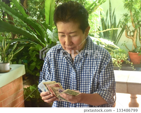Asian elder woman counting national banknote in home front yard 133486799