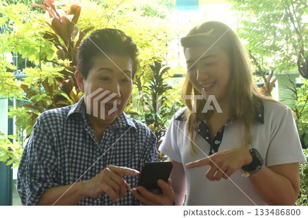 Asian elder woman and daughter to checking mobile phone in front of home 133486800