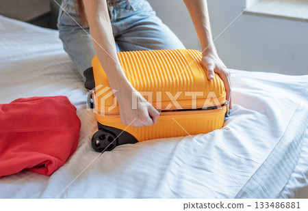 Woman packing suitcase on bed preparing for travel Woman packing suitcase on bed preparing for travel 133486881