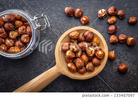 Peeled hazelnut kernels on wooden spoon on black table. Top view. 133487097