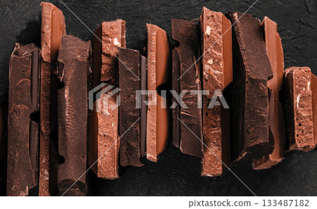 Assorted stacked chocolate bar pieces with rich textures and broken edges on dark background for premium confectionery branding and dessert advertising 133487182