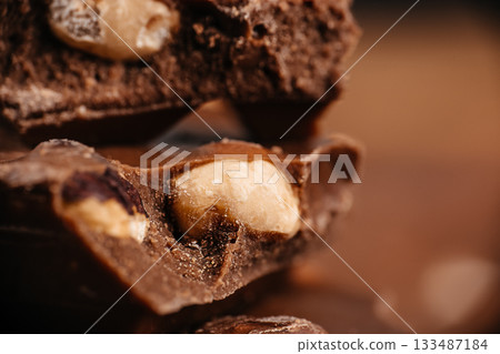 Macro view of broken chocolate pieces with whole nuts on a warm brown background ideal for dessert advertising and confectionery branding 133487184