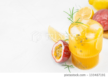 Refreshing tropical drink with passion fruit, lemon slices, ice cubes, and rosemary served in a ribbed glass on a white background. copy space 133487191
