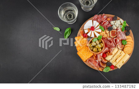 Elegant charcuterie board with assorted cheeses, cured meats, crackers, olives, figs, berries and wine on dark background with copy space 133487192