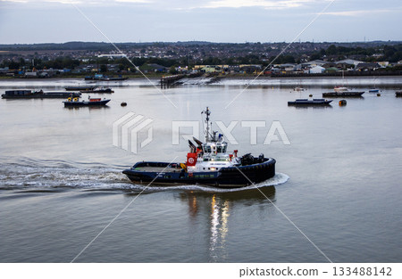 Tugboat Navigates Calm Waters With Distant Docks in the Background 133488142