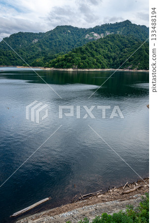 The majestic water surface and mountain ranges of Lake Okutadami in Niigata Prefecture, with driftwood along the lakeside The majestic water surface and mountain ranges of Lake Okutadami in Niigata Prefecture, with driftwood along the lakeside 133488194