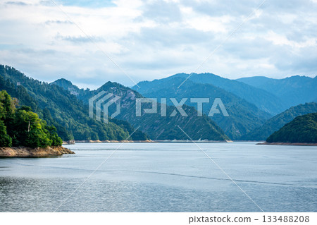 新潟縣奧田岷湖雄偉的山脈和湖面,夏末的陰天 新潟縣奧田岷湖雄偉的山脈和湖面,夏末的陰天 133488208