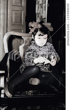 Vintage portrait of little girl with bows and velvet dress sitting in a chair. Retro photo from 1972. Vintage portrait of little girl with bows and velvet dress sitting in a chair. Retro photo from 1972. 133489830