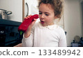 Little girl examining and eating red pepper in home kitchen 133489942