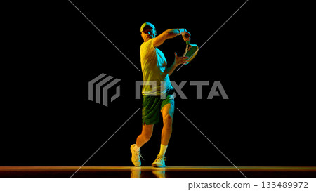 Male tennis player striking forehand with focus and precision in studio light Male tennis player striking forehand with focus and precision in studio light 133489972