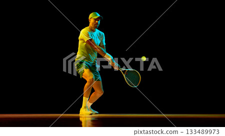 Focused tennis player returning ball with calm concentration under dramatic light 133489973