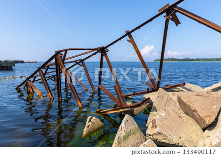 A weathered rusted metal structure extends into blue coastal waters A weathered rusted metal structure extends into blue coastal waters 133490117