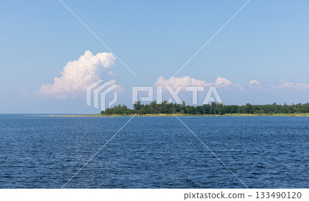A tranquil seascape featuring a distant coast, lush green trees, and a vast blue sea A tranquil seascape featuring a distant coast, lush green trees, and a vast blue sea 133490120